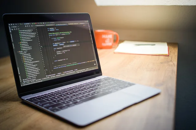 Laptop showcasing code on a desk with a notebook and mug, emphasizing a modern workspace setting. How to Build Landing Pages for a UK Small Business