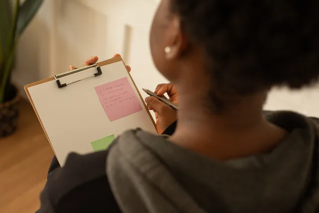 A woman writes notes on a clipboard with colorful sticky notes indoors. Pre-release checks on a landing page's claims, overall impression and testimonials
